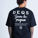 Tył T-shirtu DEQS z dużym napisem „Strive for Progress” – moda z przesłaniem