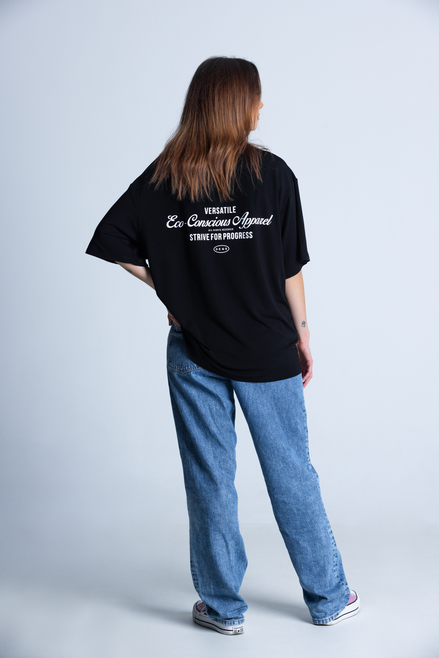 Kobieta bokiem w koszulce DEQS – stylizacja casual z nadrukiem